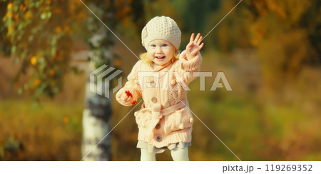 Happy little cheerful child having fun playing in autumn park in warm knitted sweater and hat 119269352
