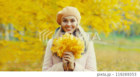 Beautiful happy smiling young woman holding yellow maple leaves with french beret in autumn park 119269353