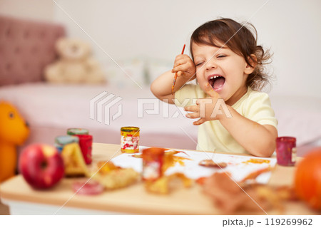happy little child girl painting autumn leaves. smiling baby girl drawing leaves in yellow paint 119269962