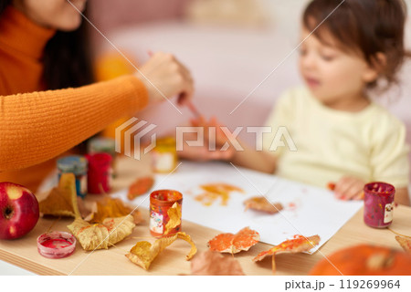 close-up, child and mom hands painting autumn yellow leaves together. happy time together at home 119269964