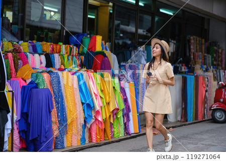 A woman is walking down a street with a colorful display of fabric 119271064