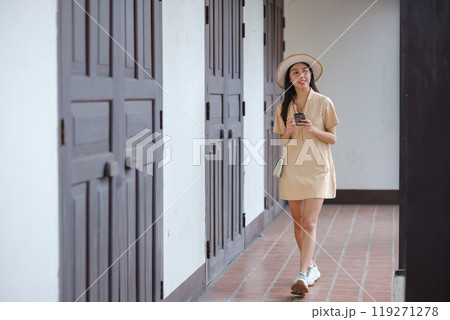 A woman is walking down a hallway with a cell phone in her hand A woman is walking down a hallway with a cell phone in her hand 119271278