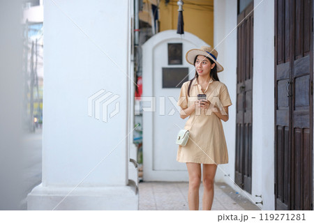 A woman in a yellow dress is walking down a street while holding a cell phone 119271281