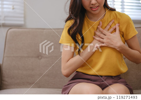 A woman in a yellow shirt is sitting on a couch with her hand on her chest 119271493