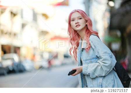A woman with pink hair is looking at her cell phone while walking down a street 119271537