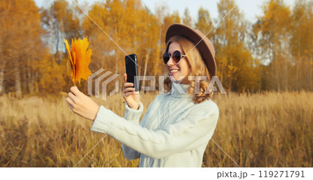 Happy smiling young woman taking pictures of yellow leaves on phone in autumn park Happy smiling young woman taking pictures of yellow leaves on phone in autumn park 119271791