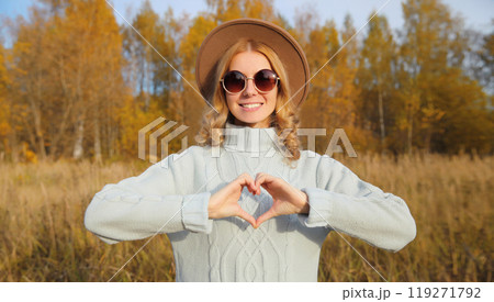 Beauty portrait of stylish happy young woman showing heart gesture, girl smiling in autumn park Beauty portrait of stylish happy young woman showing heart gesture, girl smiling in autumn park 119271792