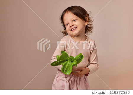 smiling child girl holding fresh green salad on beige background. healthy baby food. 119272580