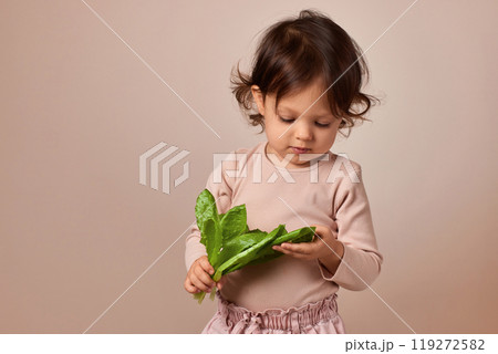 cute child girl holding fresh green salad on beige background. healthy baby food. 119272582