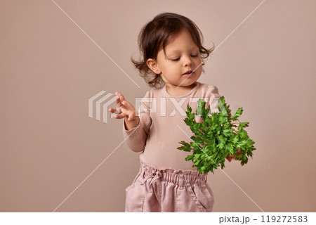 smiling child girl holding fresh green parsley on beige background. healthy baby food. smiling child girl holding fresh green parsley on beige background. healthy baby food. 119272583
