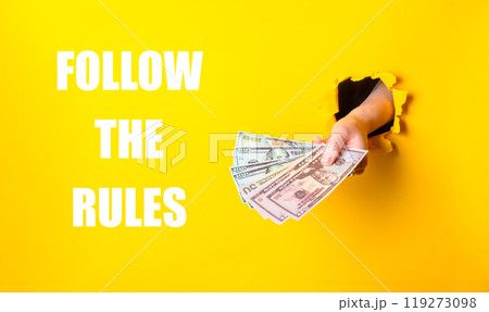 A hand holding a stack of money with the words follow the rules written below it 119273098