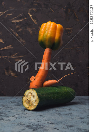A carrot is standing on top of a zucchini 119273127