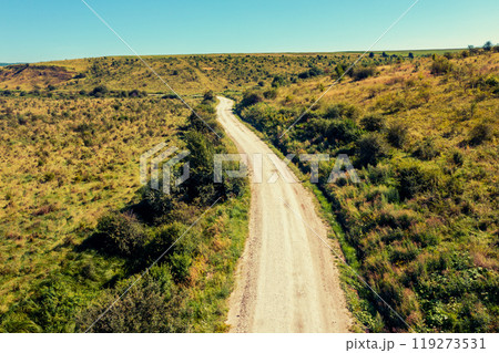 Drone view of the dirt road between hills on a sunny summer day 119273531