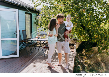 Happy family enjoying a peaceful outdoor moment on a wooden deck, surrounded by nature and sunshine 119275003