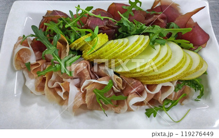 prosciutto and beef jerky with fresh pear and herbs on a large white plate prosciutto and beef jerky with fresh pear and herbs on a large white plate 119276449