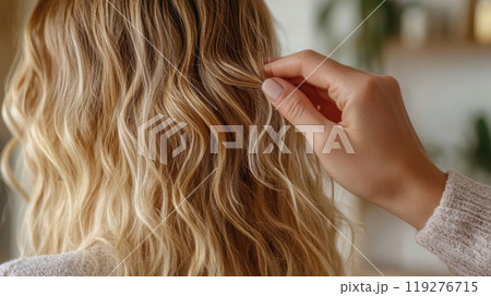 a close-up view of a person with soft, wavy blonde hair, while another hand gently holds and styles a section of the hair 119276715