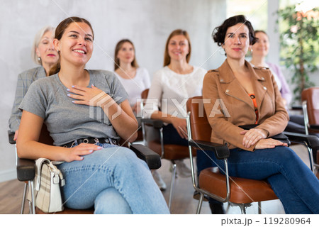 small group of women are sitting in audience, listening to lecture and laugh at amusing case small group of women are sitting in audience, listening to lecture and laugh at amusing case 119280964
