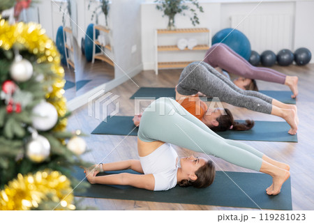 Girl teacher conducts lesson, training for girls in yoga studio and performs plow pose in New Year atmosphere Girl teacher conducts lesson, training for girls in yoga studio and performs plow pose in New Year atmosphere 119281023