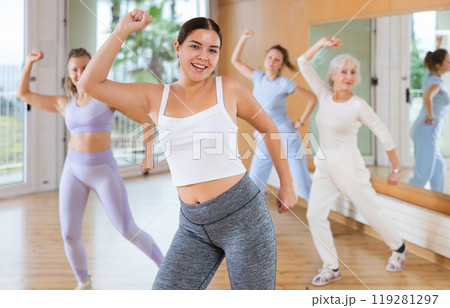 Emotional sportive female dancers of different ages in sportswear exercising new dance moves in fitness studio 119281297