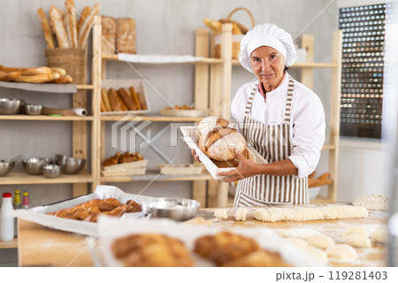 Experienced aged woman in apron working in bakery kitchen, posing with baked bread 119281403