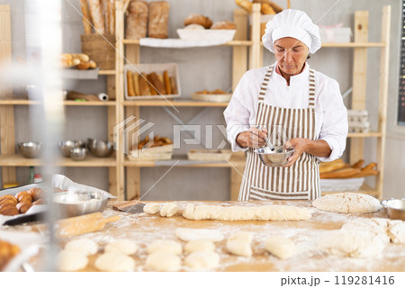 Aged female baker mixing ingredients for dough in bowl Aged female baker mixing ingredients for dough in bowl 119281416