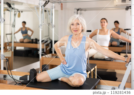 Elderly woman in sportswear training pilates performer bed in gym Elderly woman in sportswear training pilates performer bed in gym 119281436