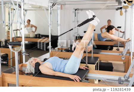 Elderly woman performing set of pilates exercises on reformer 119281439