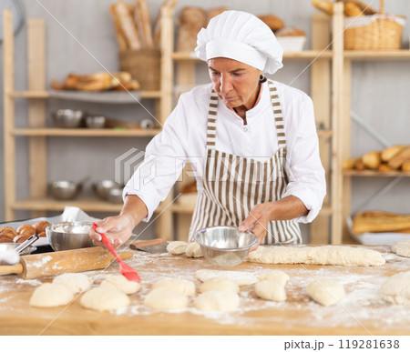Aged woman baker buttering pieces of dough in bakery 119281638
