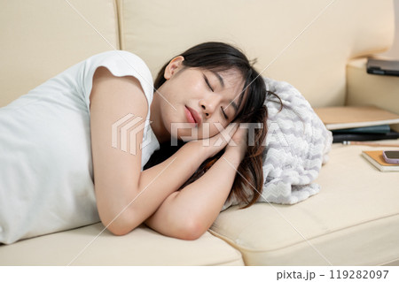 A pretty, happy young Asian woman in comfy clothes is taking a nap on a sofa in the living room. 119282097