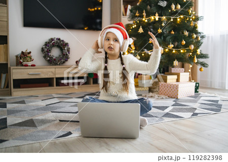Little girl in headphones enjoying Christmas music near tree Little girl in headphones enjoying Christmas music near tree 119282398