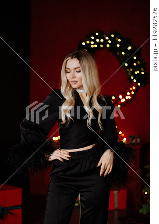 Woman in black satin blouse with feathers on her hands posing in Christmas interior of living room. 119282526
