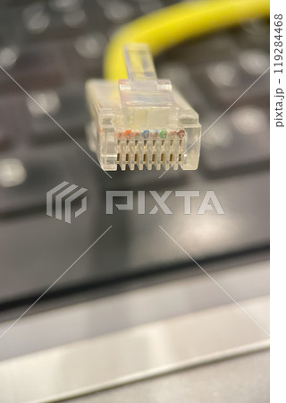Ethernet Cable Close-up.A close-up photo of an Ethernet cable connector, showcasing the eight colored wires inside. The cable is yellow and is positioned above a laptop keyboard. Ethernet Cable Close-up.A close-up photo of an Ethernet cable connector, showcasing the eight colored wires inside. The cable is yellow and is positioned above a laptop keyboard. 119284468