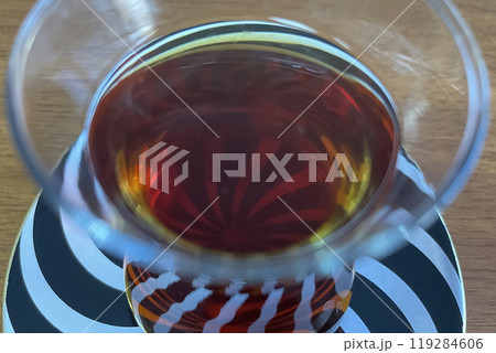 A close-up photo of a glass of dark tea, possibly Turkish tea, resting on a saucer with a swirling black and white pattern. A close-up photo of a glass of dark tea, possibly Turkish tea, resting on a saucer with a swirling black and white pattern. 119284606
