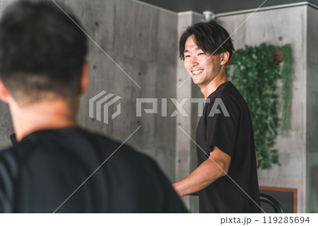 ジムでトレーニング中にトレーニング仲間と笑顔で会話する若いアジア人男性 119285694