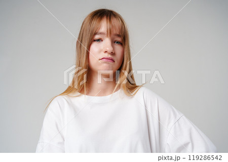 A young girl with long hair looks unimpressed against a plain background A young girl with long hair looks unimpressed against a plain background 119286542