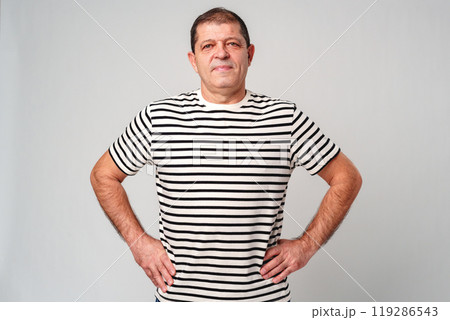 A man stands confidently in a striped shirt, casual jeans with a neutral background 119286543