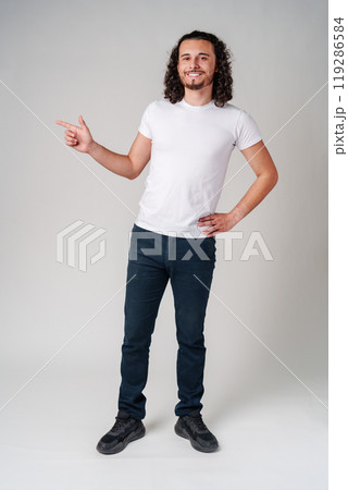 Cheerful young man presenting with outstretched hand in a studio setting Cheerful young man presenting with outstretched hand in a studio setting 119286584