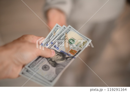 A hand passes hundred dollar bills to another person 119291164