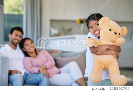 Family, kid and teddy bear with hug in home, having fun and bonding with mother and father gift. Support, care and love of happy parents playing with girl holding toy with sofa in house living room 119292703
