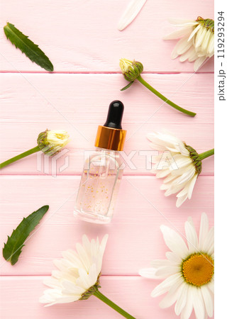 Essential oil in glass bottle with fresh chamomile flowers on pink background. 119293294