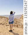 A woman is standing alone in the vast desert, curiously gazing at the distant mountains that rise majestically on the horizon 119295247