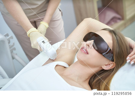Woman receiving laser hair removal treatment on armpit in a clinic setting 119295856