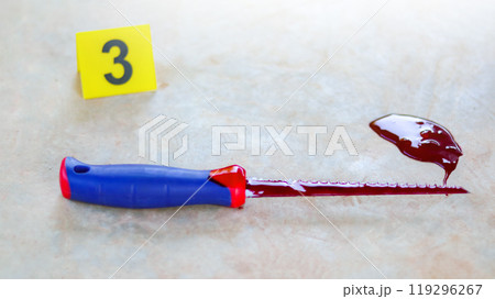 A bloodstained stainless steel handsaw lying on a concrete floor, with a blurred yellow marker number 3 and scattered blood drops, symbolizing a violent crime scene under investigation. A bloodstained stainless steel handsaw lying on a concrete floor, with a blurred yellow marker number 3 and scattered blood drops, symbolizing a violent crime scene under investigation. 119296267