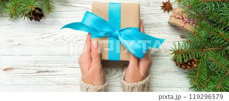 Woman hands give wrapped christmas handmade present in paper with blue ribbon. Present box on holiday on white wooden table, top view Woman hands give wrapped christmas handmade present in paper with blue ribbon. Present box on holiday on white wooden table, top view 119296579