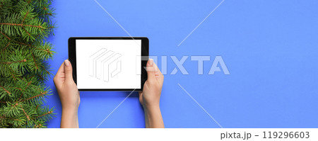 female hands with tablet computer on purple christmas background. Xmas tree branch top view 119296603