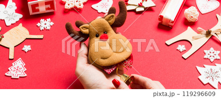 Top view of reindeer in female hands on red background. Christmas decorations. New Year holiday concept Top view of reindeer in female hands on red background. Christmas decorations. New Year holiday concept 119296609