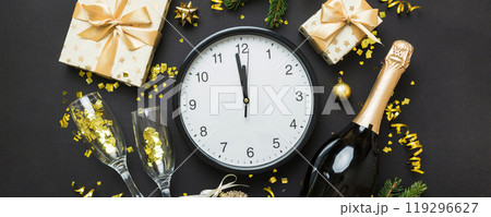 New year celebration concept with a bottle of champagne and two glasses toasting. Christmas gift box, alarm clock and fir tree branch on colored table. Top view Copy space 119296627