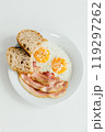 A pristine white plate beautifully topped with delicious eggs, crispy bacon, and goldenbrown bread slices that complement the meal 119297262