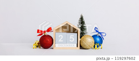 25 december. Christmas composition on colored background with a wooden calendar, with a gift box, toys, bauble copy space 25 december. Christmas composition on colored background with a wooden calendar, with a gift box, toys, bauble copy space 119297602