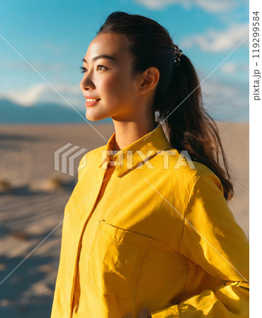 砂漠の夕日を浴びた女性。黄色の服を着ている。 119299584